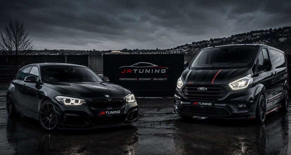 Two black tuned vehicles displayed side-by-side on wet pavement with JR Tuning branding sign behind them under stormy sky
