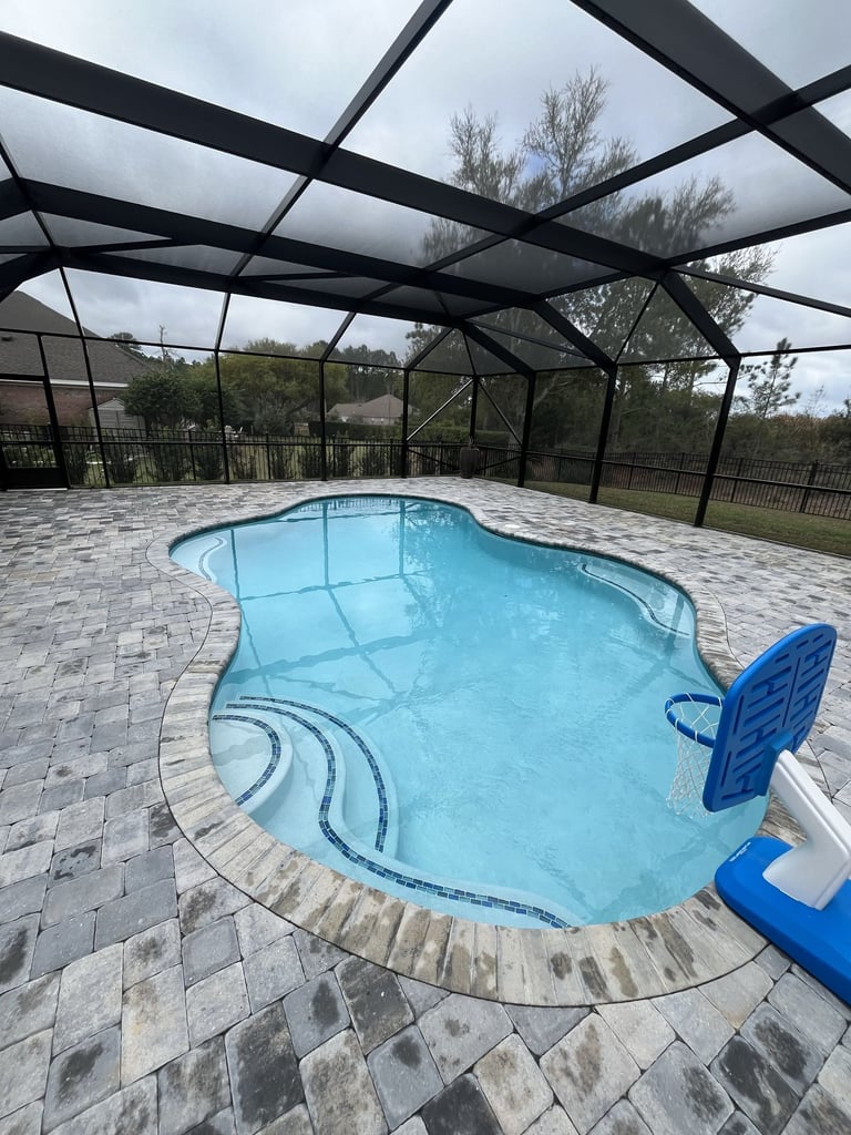 Empty swimming pool with blue water enclosed by black mesh screen cage under cloudy sky