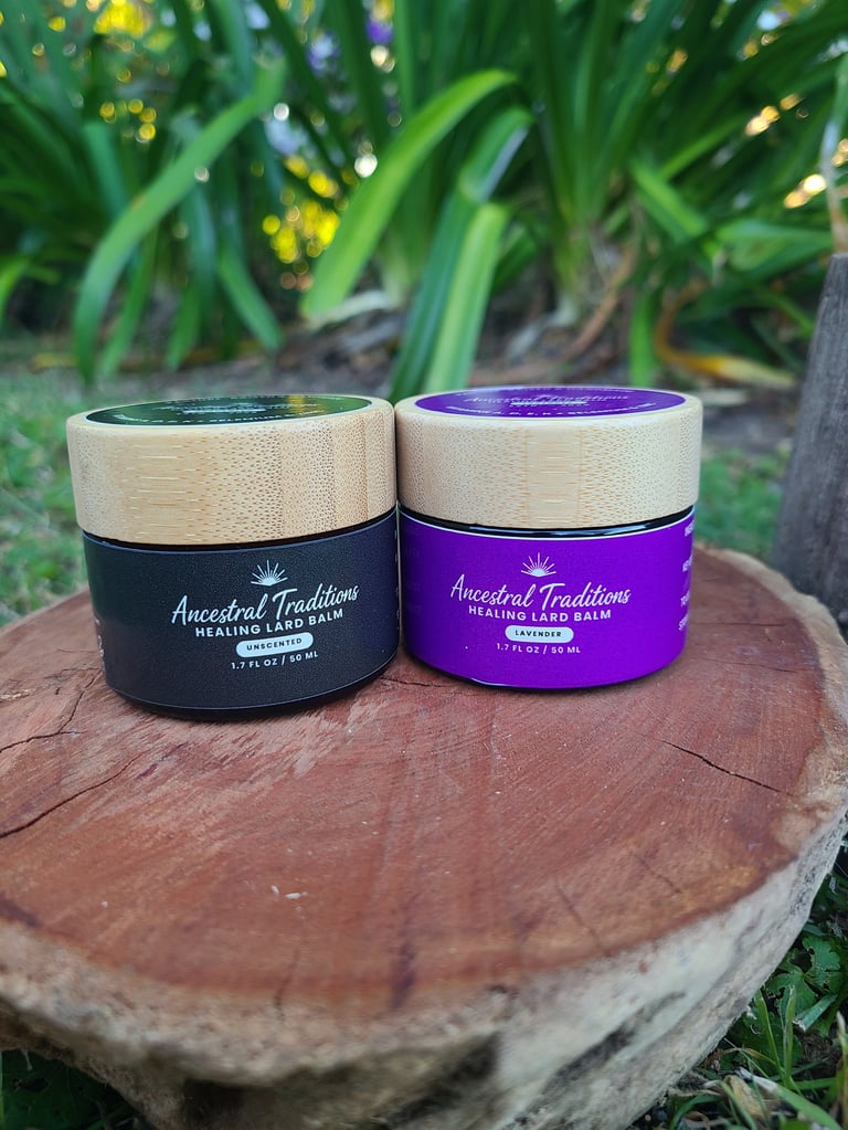 Close-up of Ancestral Traditions Healing Lard Balm jars on a wooden platform surrounded by grass and green foliage