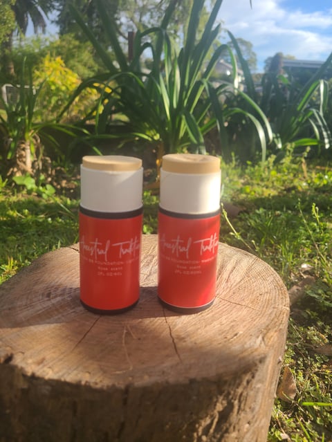 Two red and white insulated Ancestral Traditions BB Foundation tubes (Light and Medium Coverage) sitting on a wooden tree stump in a sunny garden
