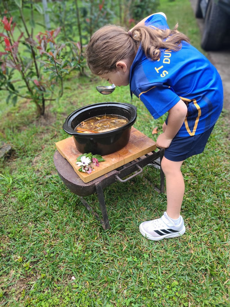 Margarita's daughter in a scout uniform tasting food from a pot during a family outdoor cooking activity