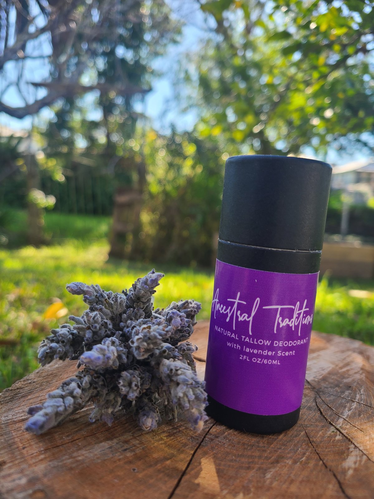 Purple natural tallow deodorant stick with lavender scent next to dried lavender flowers on a wooden surface in a garden setting