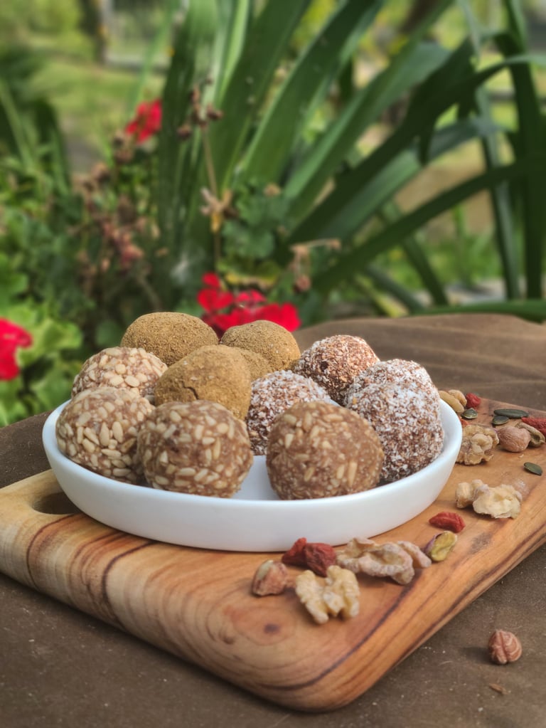 Bowl of homemade energy balls with nuts and cocoa on wooden board in garden setting with red flowers