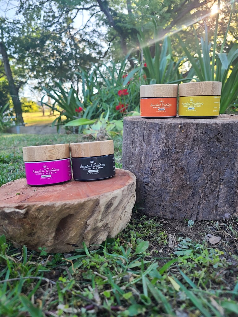Four colored jars of Ancestral Traditions Healing Lard Balm displayed on tree stumps in a garden setting