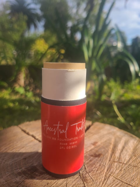 Red Ancestral Traditions Tallow BB Foundation Light tube with white cap and beige top on a wooden surface in a sunlit garden