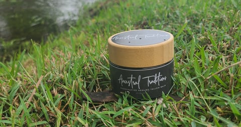 Ancestral Traditions unscented tallow moisturiser jar with wooden lid and black label on green grass outdoors