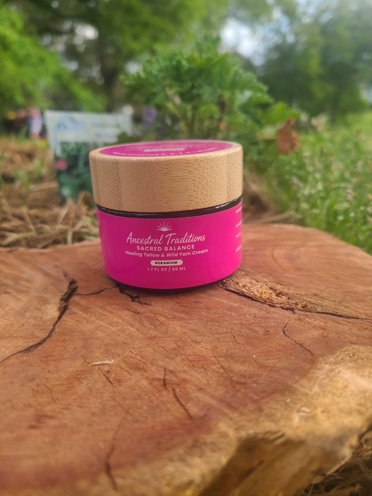 Pink and natural wood jar of Ancestral Traditions Sacred Balance product on brown wood surface with blurred garden background