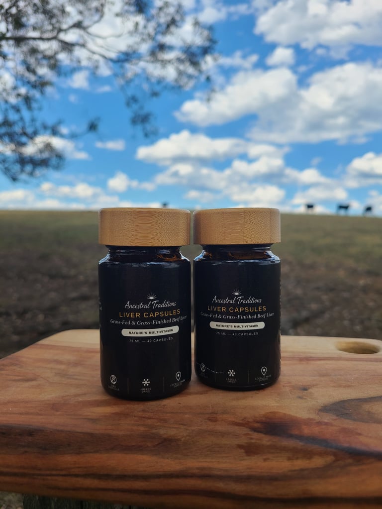 Two dark glass bottles with wooden caps labeled Liver Capsules on a wooden surface with rural landscape and blue sky in background
