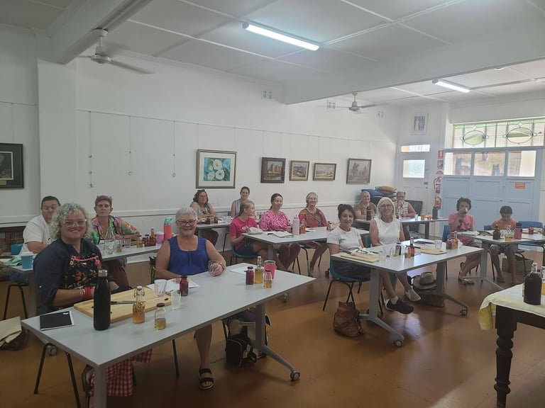 Group of people gathered in a bright classroom with white walls, seated at tables during a community workshop