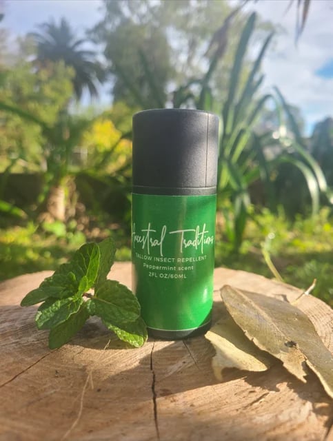 Green insect repellent bottle with peppermint scent displayed on wood with fresh mint leaves and tropical plants in background