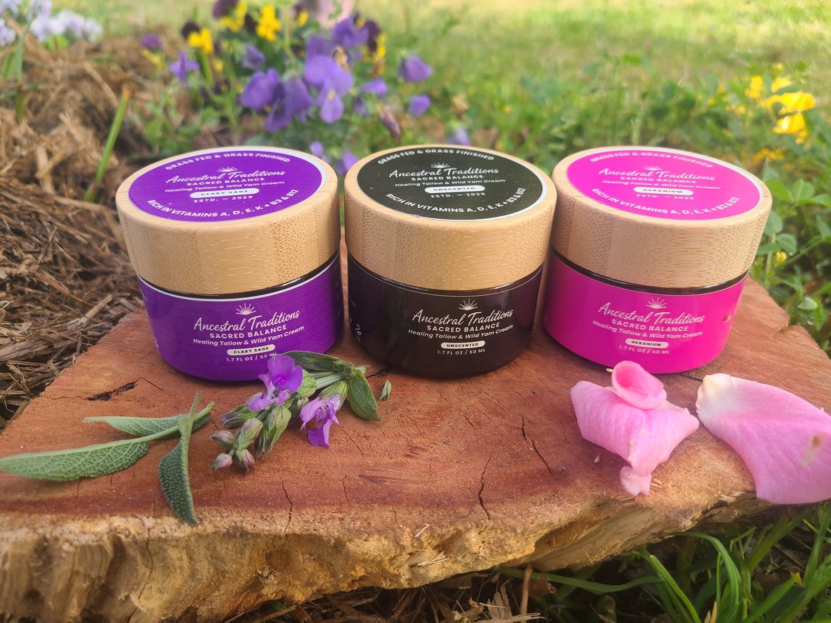 Three Ancestral Traditions Sacred Balance jars with purple, black, and pink labels on a wooden slab in a garden setting with flowers and herbs