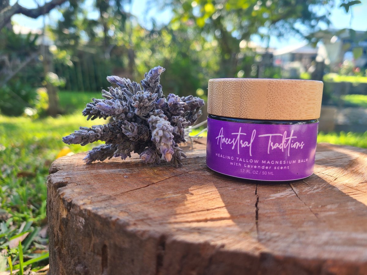Purple Ancestral Traditions Healing Tallow Magnesium Balm with lavender scent next to dried lavender on a wooden tree stump in a sunny garden