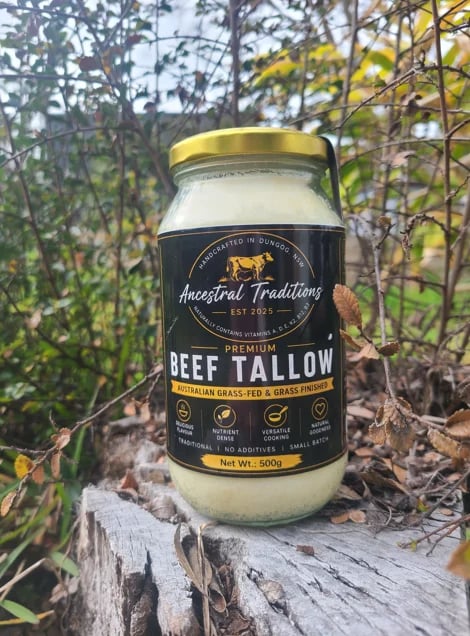Jar of Ancestral Traditions premium beef tallow sitting on a log in an outdoor garden setting