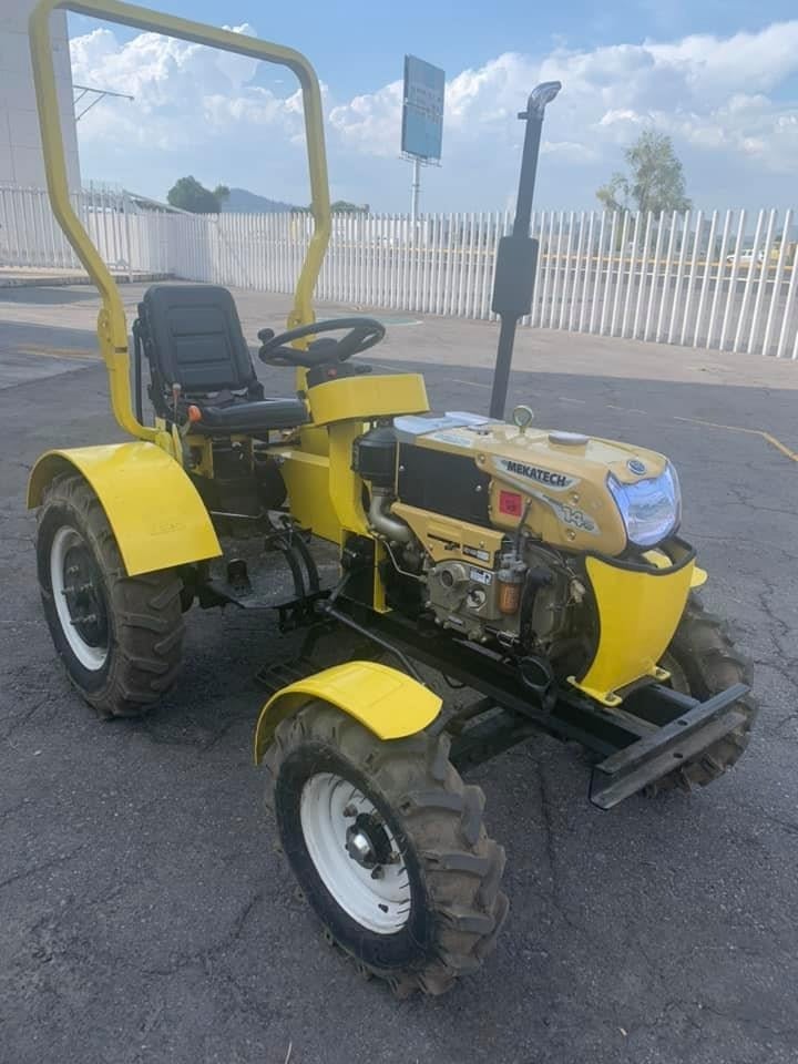 Yellow compact tractor with diesel engine parked in lot near white fence and blue sky