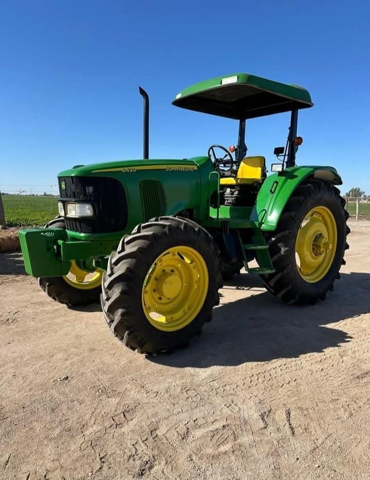 Green and yellow John Deere farm tractor with canopy parked on dirt road against clear blue sky