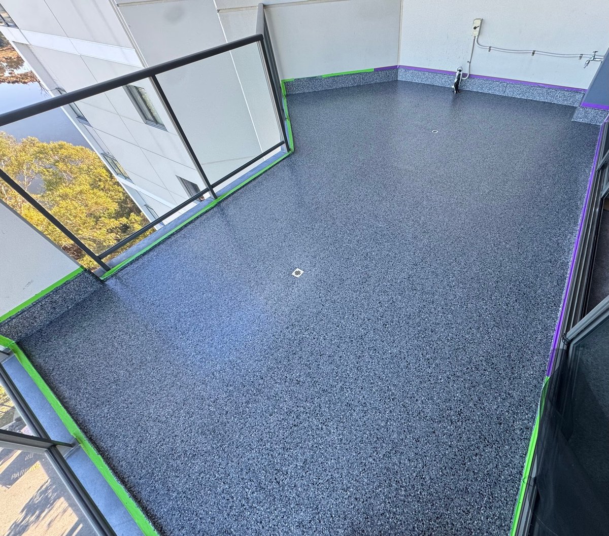 Outdoor balcony with a dark grey speckled flake floor, green and purple painter's tape along the edge