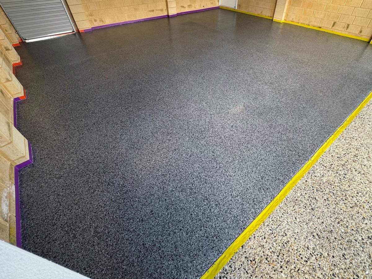 Dark charcoal speckled epoxy floor with yellow safety border trim in a finished garage