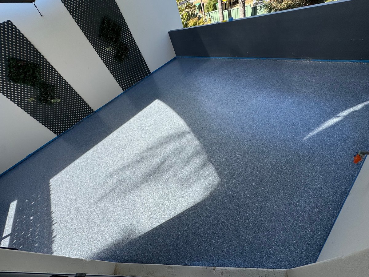 Bright outdoor balcony with a smooth blue-grey epoxy floor and decorative metal screens