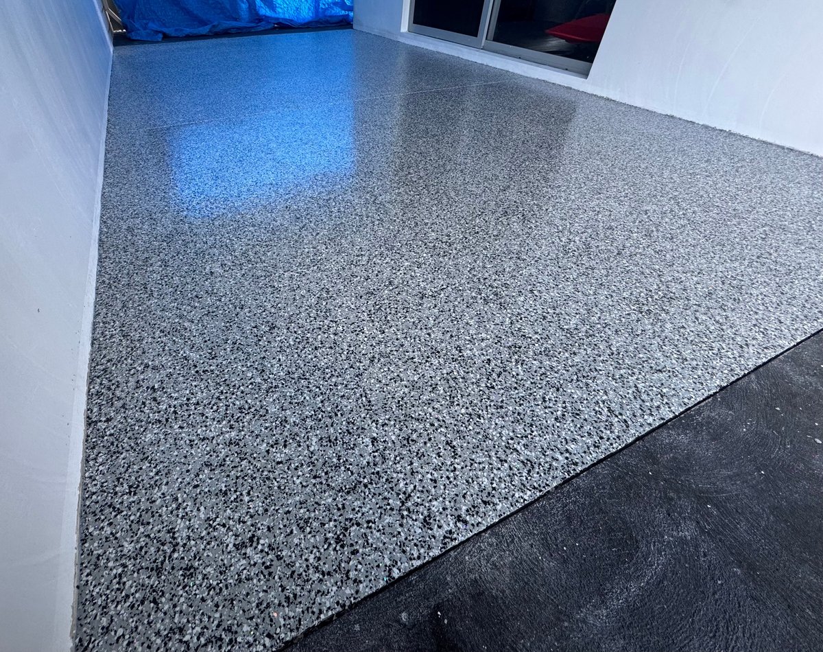 Garage with a half-finished grey speckled flake floor and blue ambient lighting