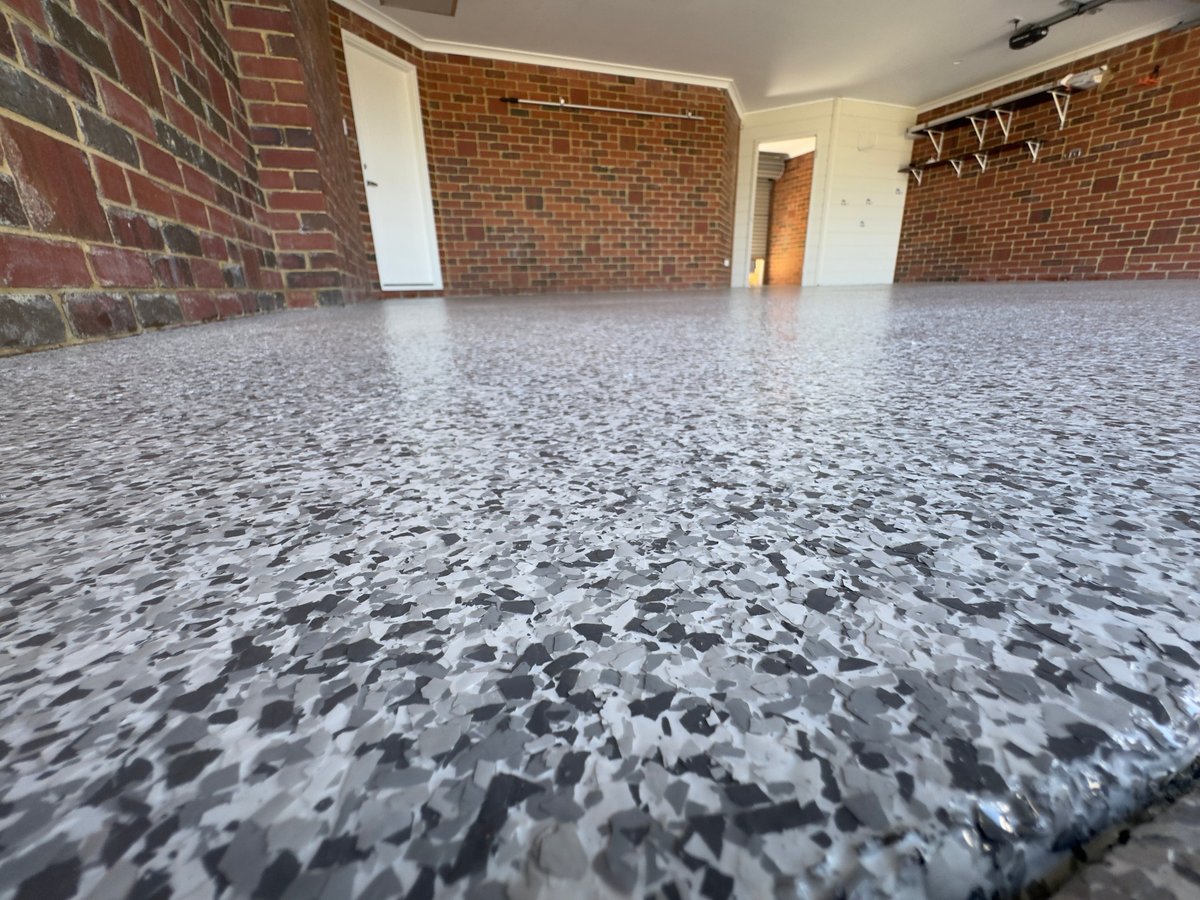Empty garage with a fresh grey speckled flake floor and exposed brick walls