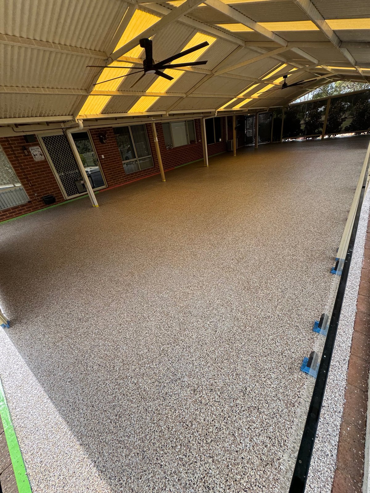 Covered carport with a fresh grey speckled flake floor, brick wall and corrugated roof