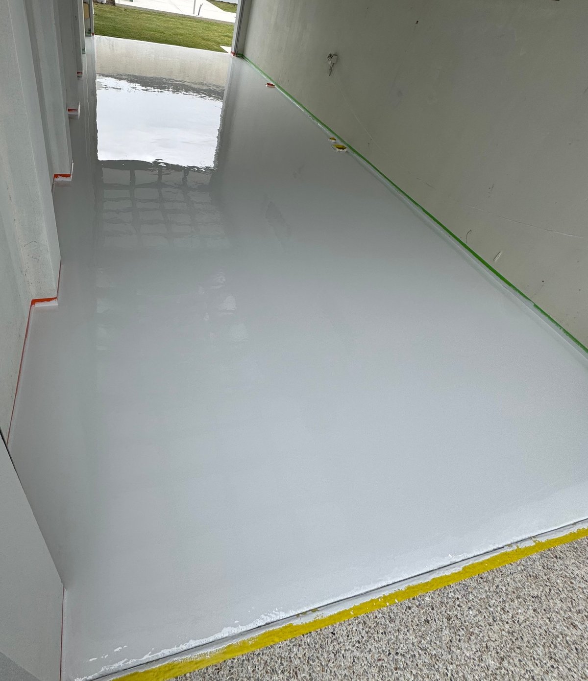 Garage mid-install with fresh white epoxy floor, open door and yellow marking tape