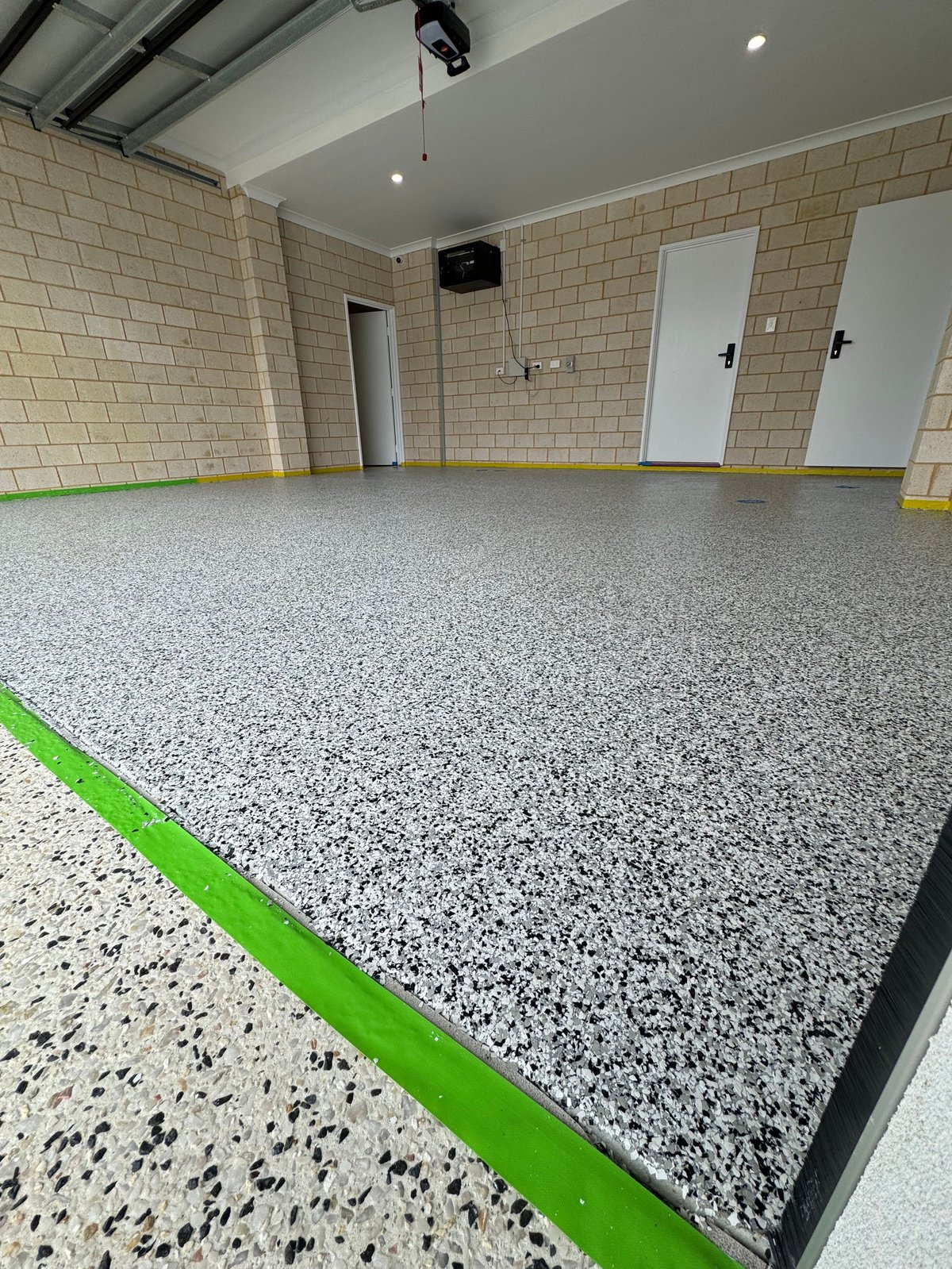 Empty garage with a fresh grey speckled flake floor, brick walls and green trim
