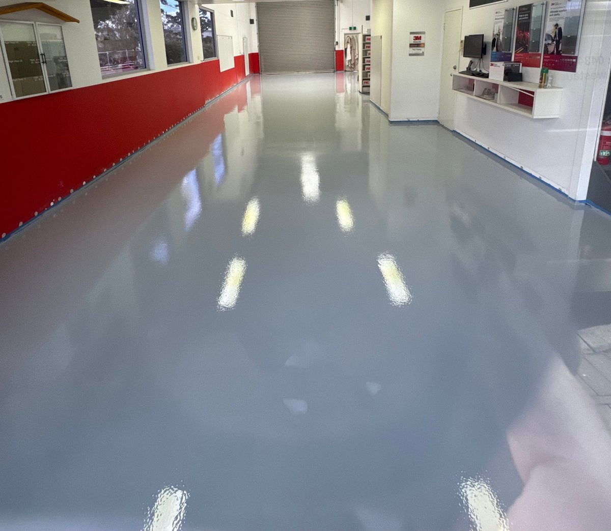 Polished grey epoxy floor in a commercial lift lobby with red feature wall and bright lighting