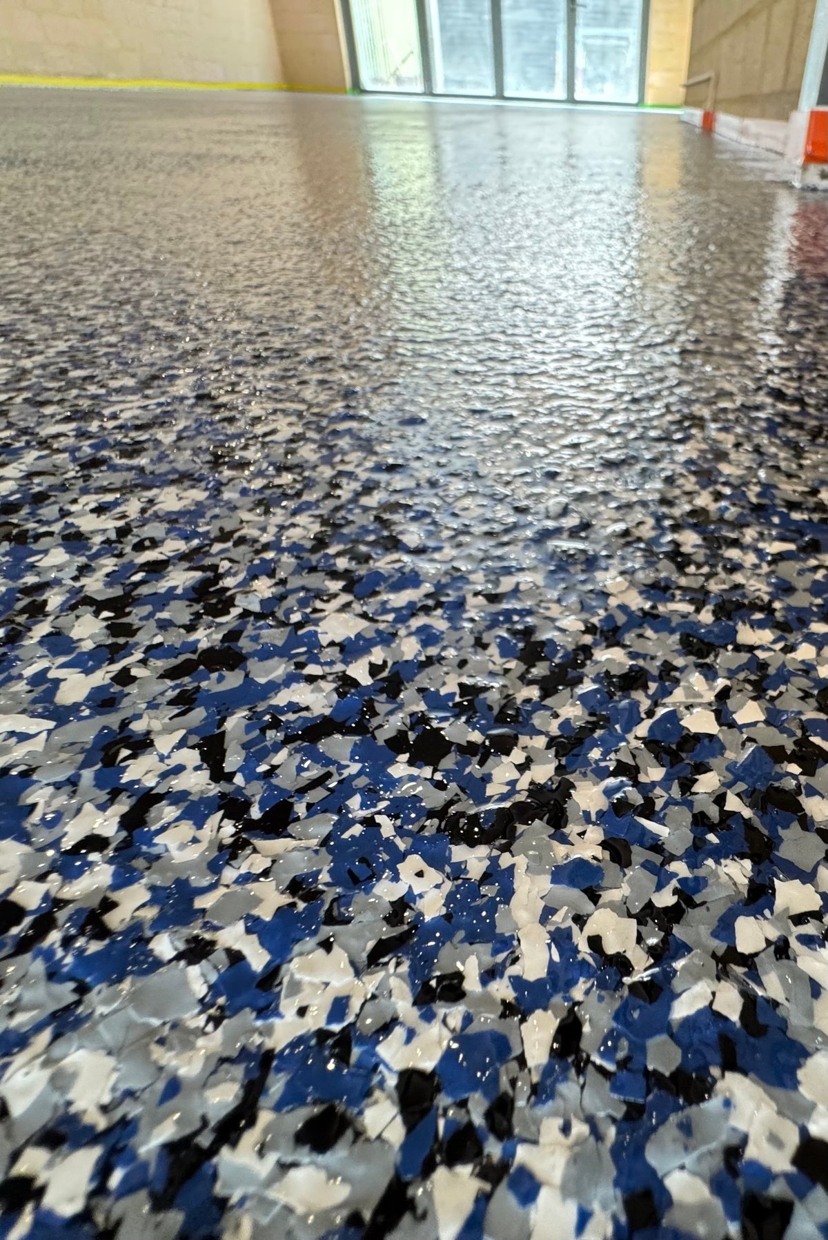Glossy blue, white and black speckled flake floor in an empty interior with glass doors