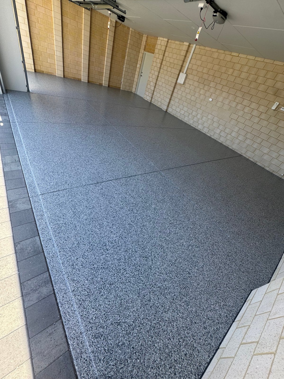 Empty garage with a polished grey flake floor, cream brick walls and roller door track