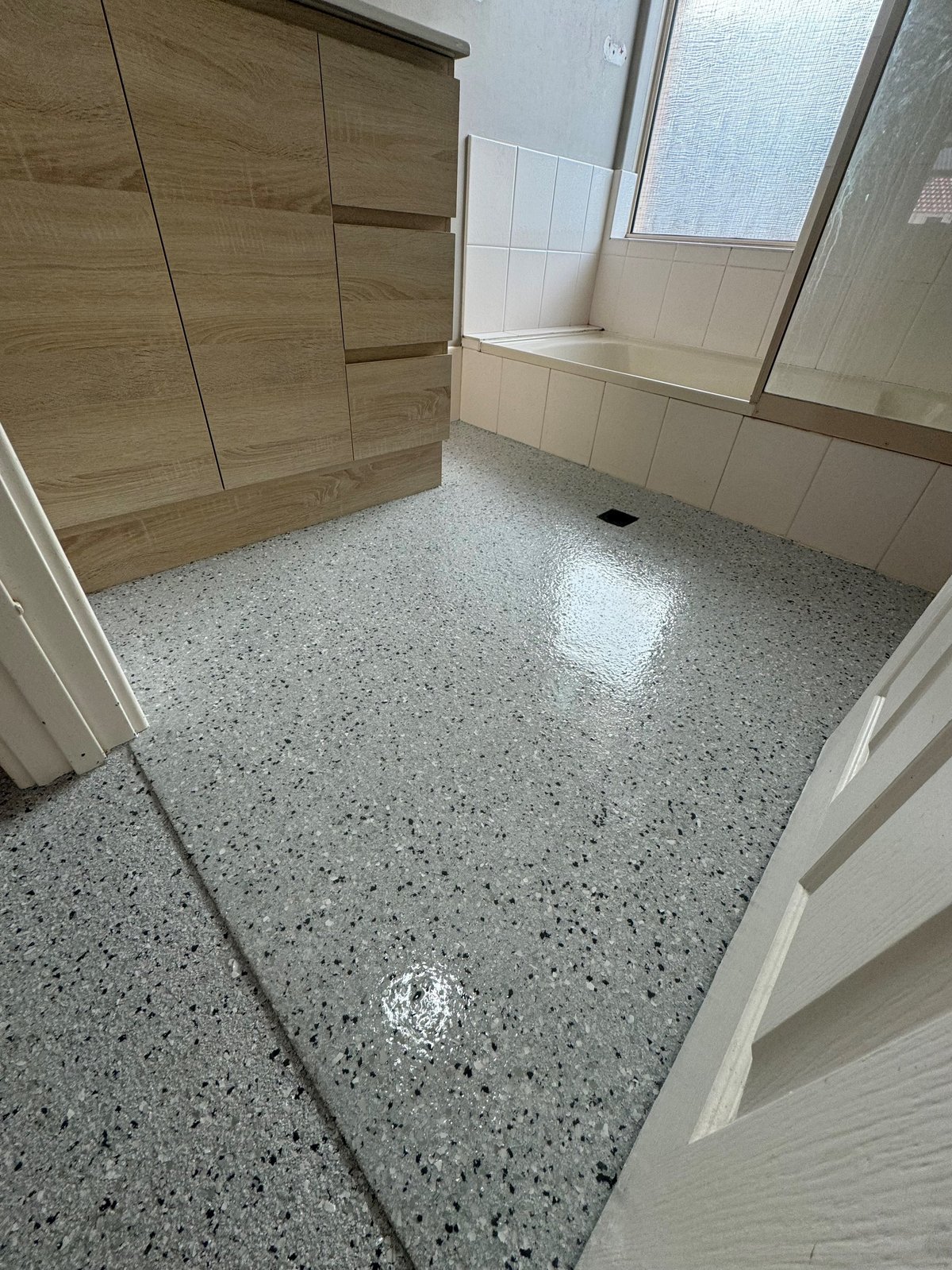 Modern bathroom with a smooth grey flake epoxy floor, timber vanity and glass shower