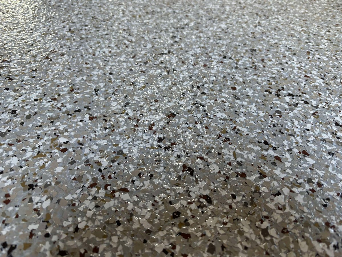 Close-up macro of a glossy grey flake epoxy floor showing black, white and gold aggregate