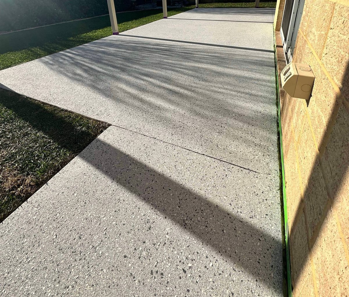 Epoxy-finished patio alongside a yellow brick wall with painter's tape and an electrical box