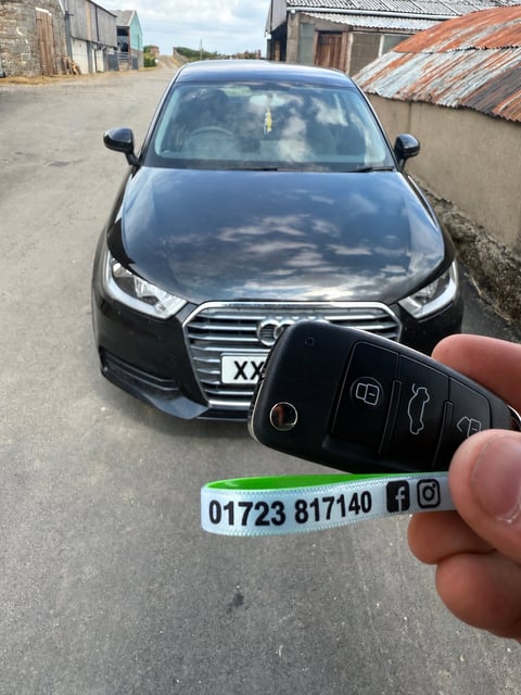 Black Audi A1 parked in a farmyard near Whitby, new key fob held in the foreground with Scarborough Auto Locksmith lanyard showing 01723 817140