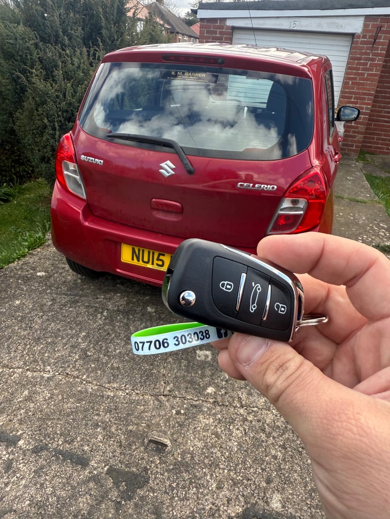 Hand holding a red Suzuki car key fob in front of a red Suzuki Celerio vehicle