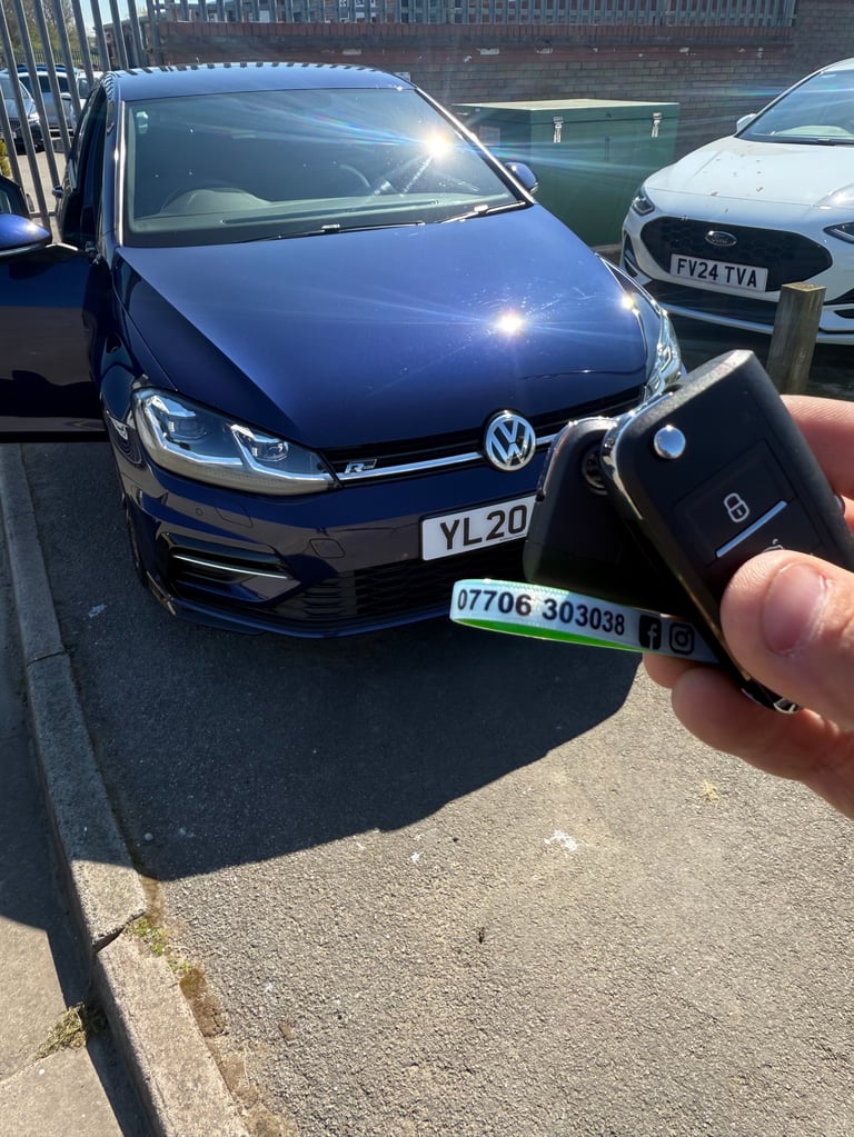 Hand holding car key fob in front of a blue Volkswagen Golf in a parking lot