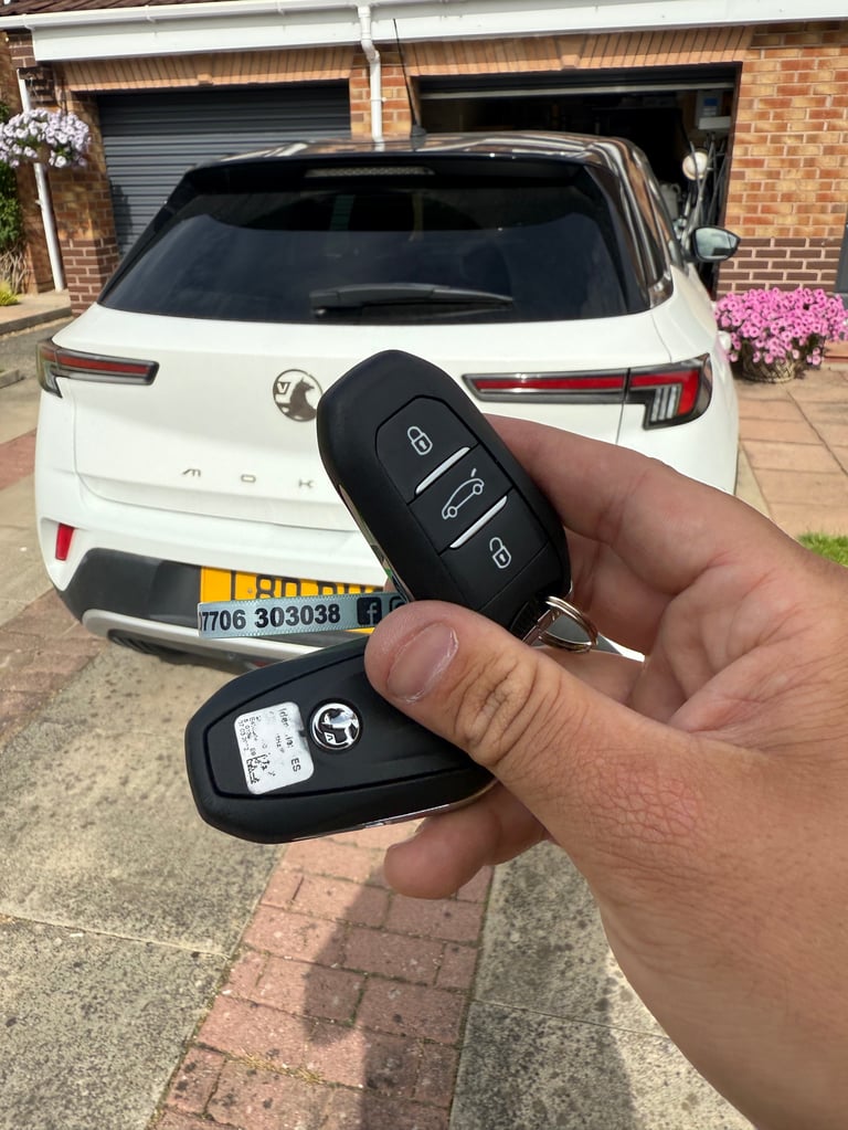 Hand holding a black car key fob in front of a white Alfa Romeo SUV parked in a driveway