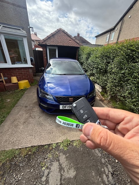 New SEAT key held in front of a blue SEAT Leon on a Scarborough driveway