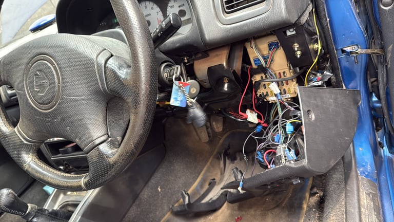 Car dashboard with steering wheel and exposed wiring, electronic components visible inside vehicle interior