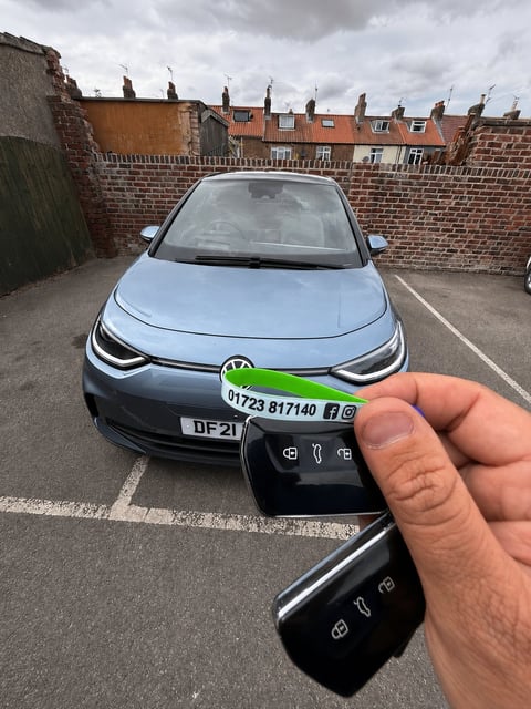 Silver and black 2021 VW ID.3 electric car in a workshop yard in Driffield. Fresh proximity smart keys held in the foreground with green Scarborough Auto Locksmith lanyard showing 01723 817140.
