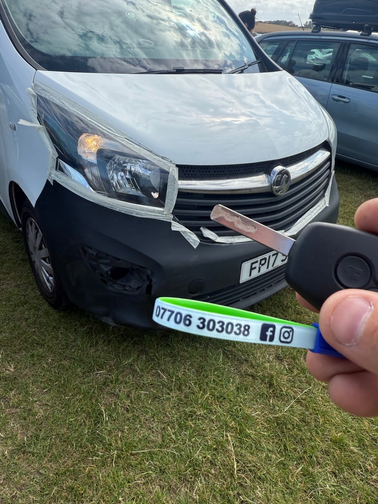Hand holding white and green business card or label in front of white and black commercial van on grass
