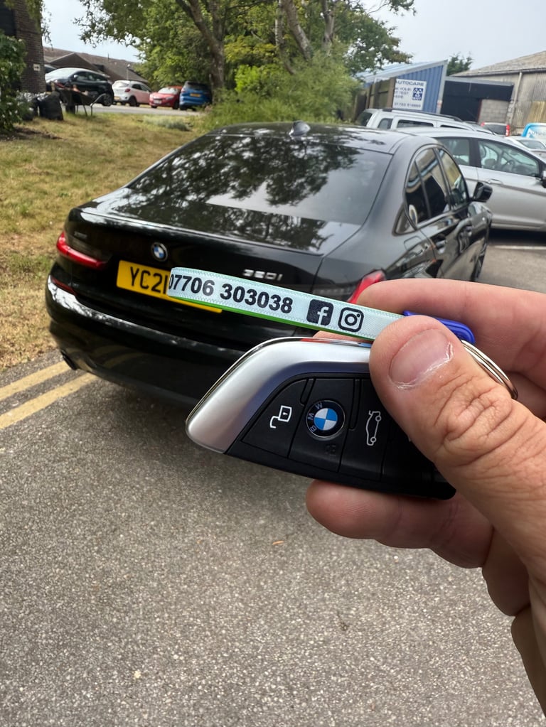 Person holding a BMW car key fob in front of a black BMW sedan with license plate visible