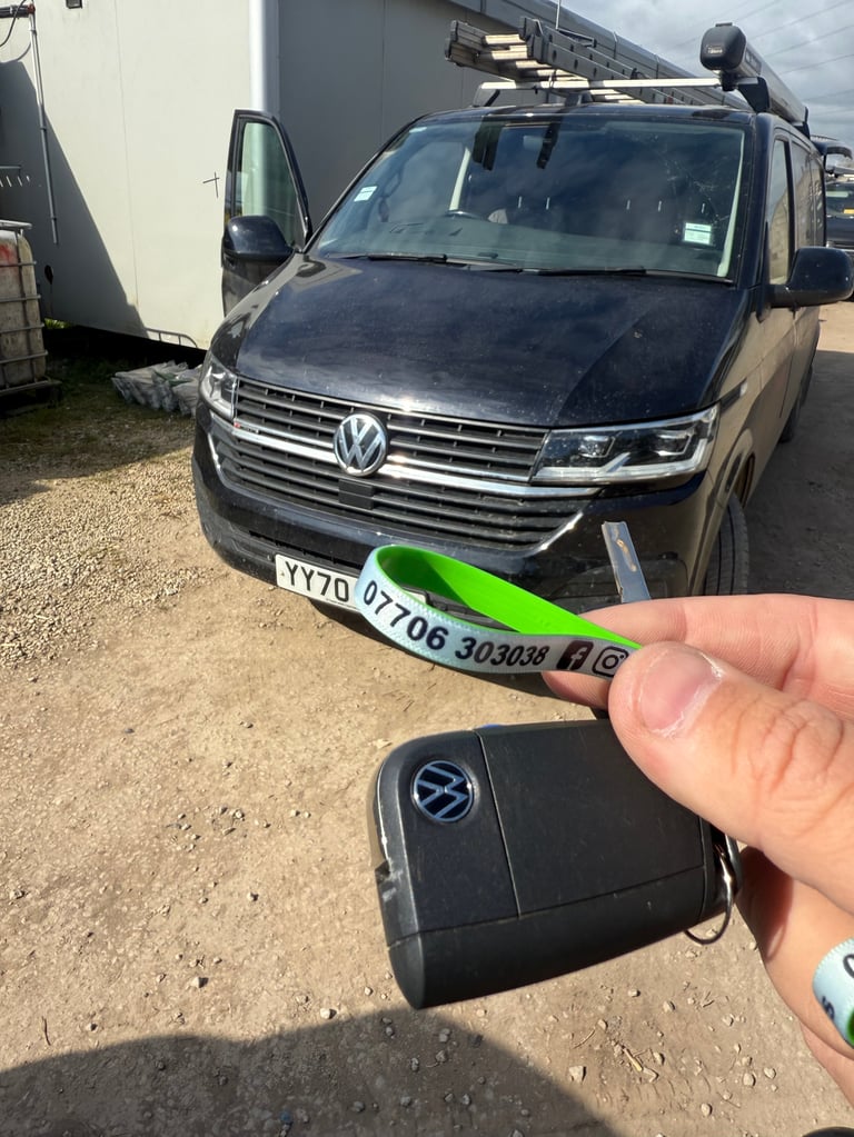 Hand holding a black Volkswagen key fob with vehicle registration plate and dark SUV in background at a lot