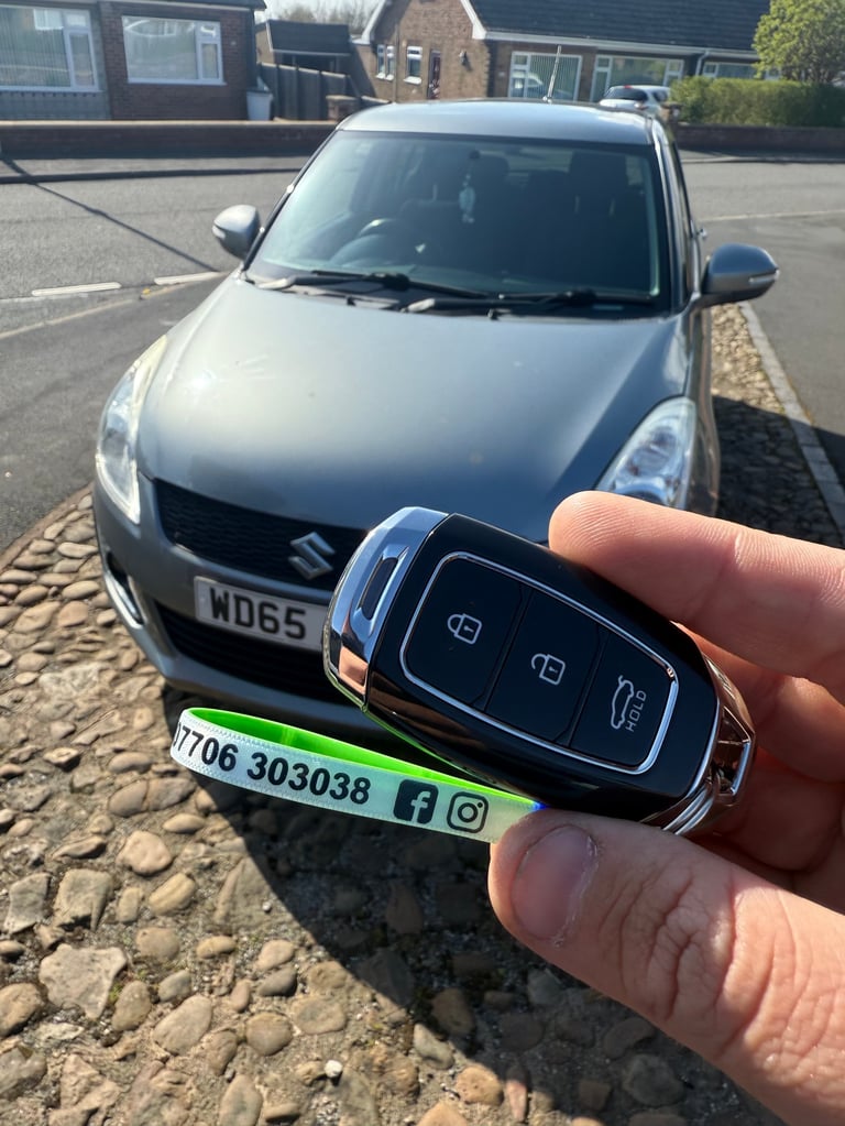 Person holding a car key fob in front of a silver Suzuki hatchback parked on a residential street