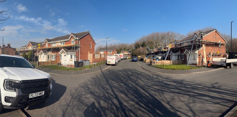 Street view of residential area with brick houses, parked vehicles, bare trees, and clear blue sky