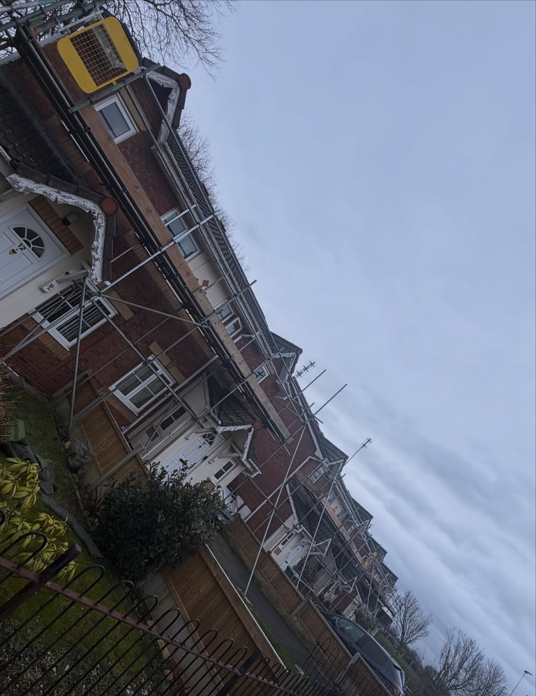 Red brick house with white trim and solar panel on roof, viewed from low angle with bare trees and overcast sky