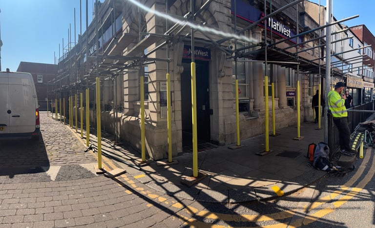 Construction site with metal scaffolding, yellow safety barriers, and a worker in high-visibility vest on a city street