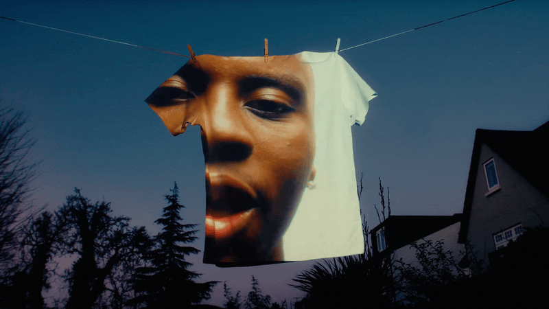 Large inflatable head sculpture displayed outdoors at dusk against a blue sky, with a residential house and trees visible below