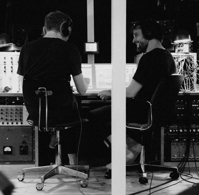 Two men in a recording studio working at synthesizers and audio equipment, black and white photograph