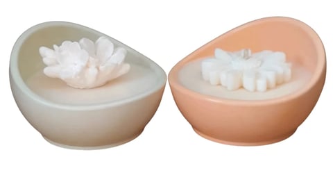 Two decorative bowls containing white wax flowers, one in beige and one in peach color